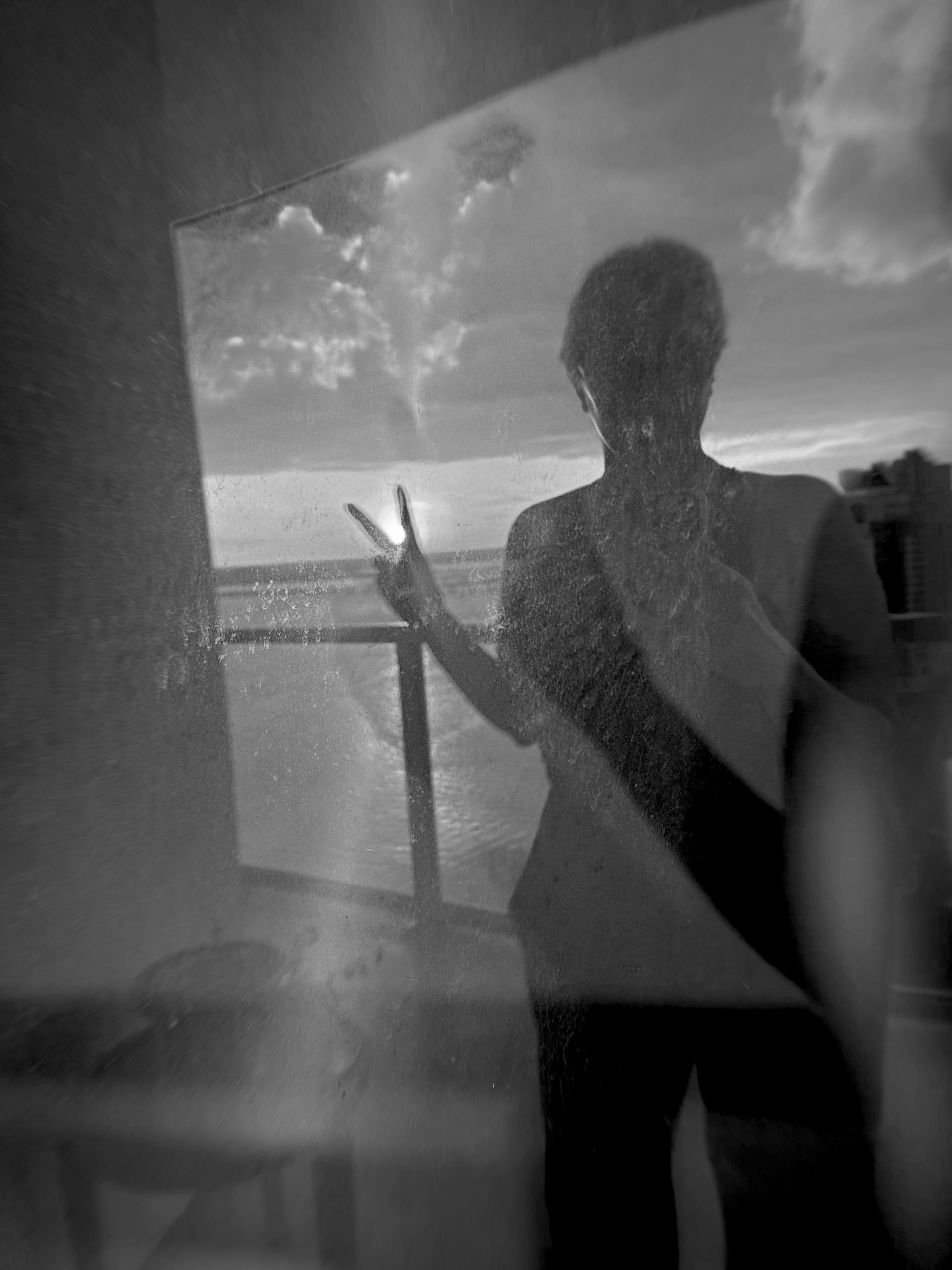 Sunset in reflected dirty window with my silhouette doing the peace symbol sunshine cutting through my fingers iPhone black and white filter.