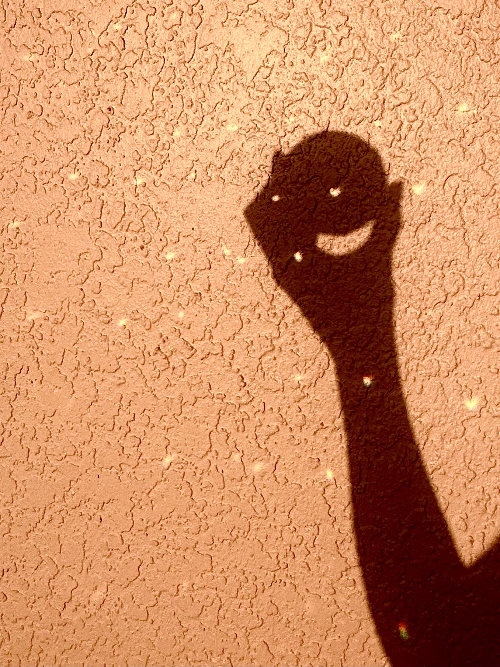 My arm holding a ball in shadow. triangles of light dancing around. A pink peach stucco wall. There’s. Rainbow on my arm too.