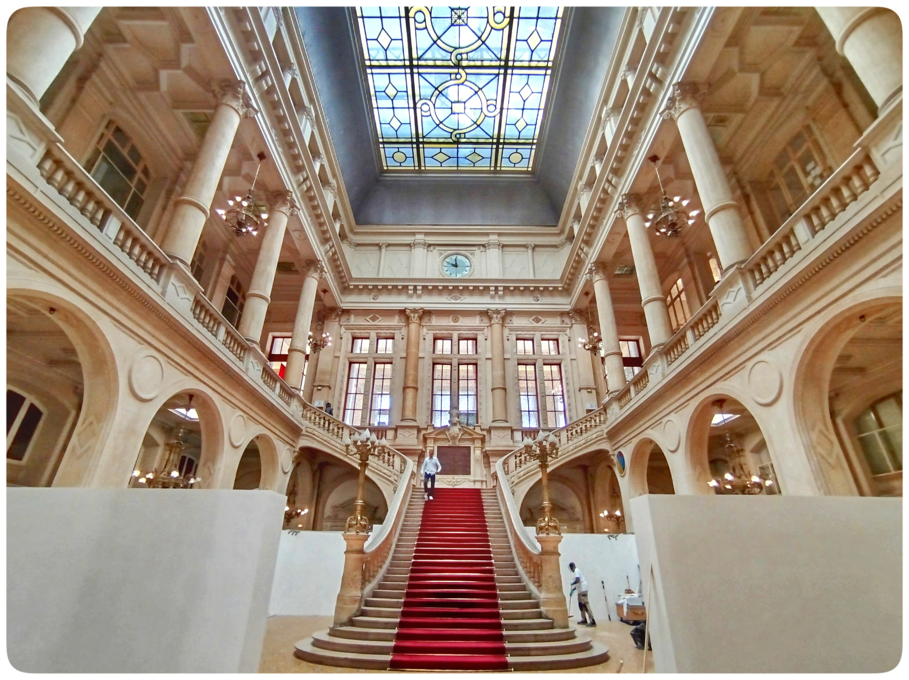 The photo shows the massive entrance hall of the local town hall of the 10th arrondissement of Paris, France.
The town hall of the 10th arrondissement is located at 72 Rue du Faubourg Saint-Martin.
It was built between 1892 and 1896 by French architect Eugène Rouyer and was by far the most expensive town hall of all 20 town halls in Paris.
It was inaugurated on January 28, 1896 in the presence of the President of the Republic, Félix Faure, a native of the district.
The imposing entrance hall is designed in the form of an atrium. It is illuminated by a skylight in the ceiling. Opposite the entrance is the monumental grand staircase, which leads to the ballroom and wedding hall on the second floor. Halfway up, the staircase splits into a right and left wing.
The current mayor of the 10th arrondissement is Alexandra Cordebard since 2017.