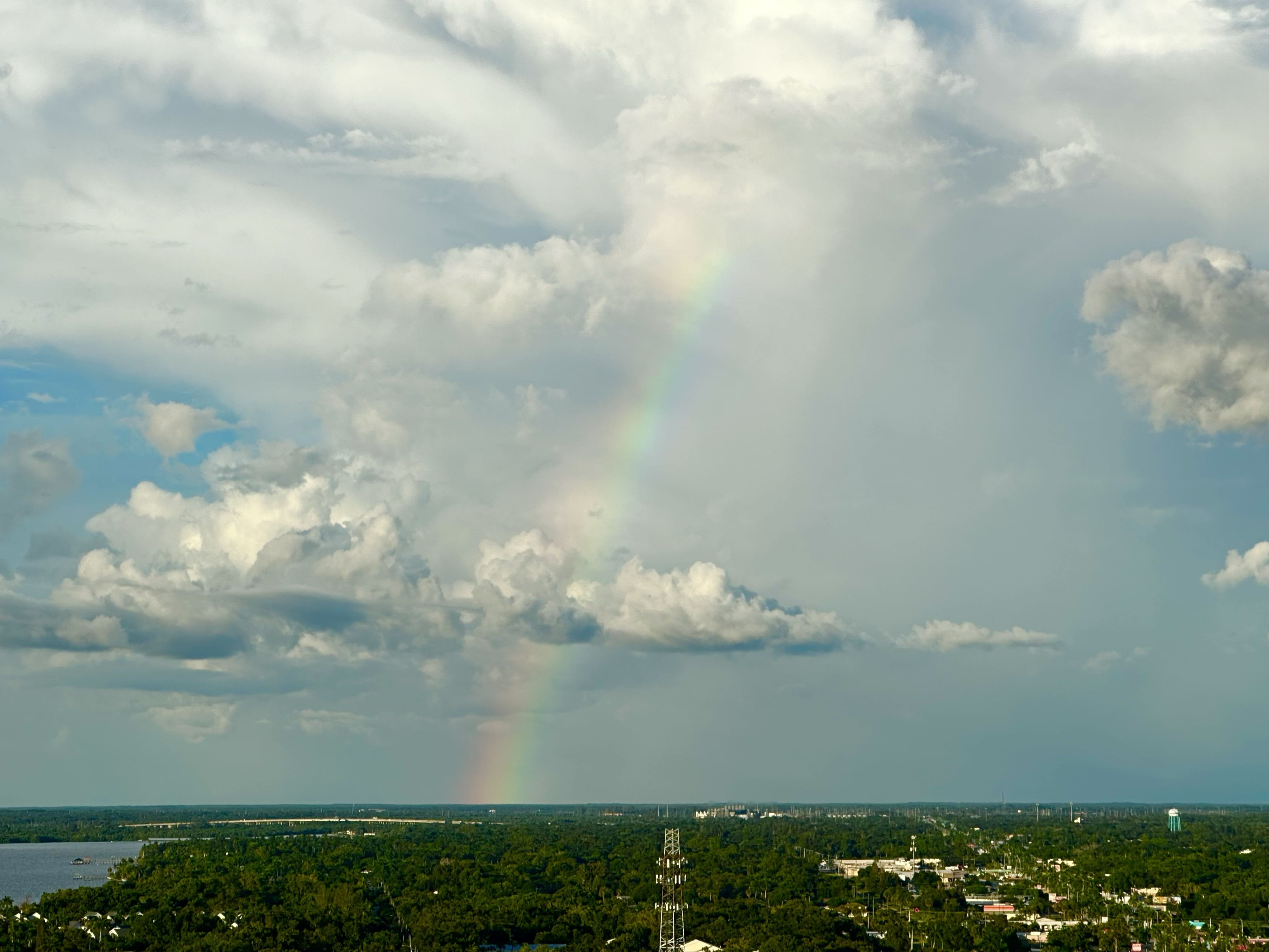 Rainbow in the sky that shoots almost straight into the sky. Blue sky clouds green landscape